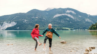 Older couple holding hands in water with mountains in background